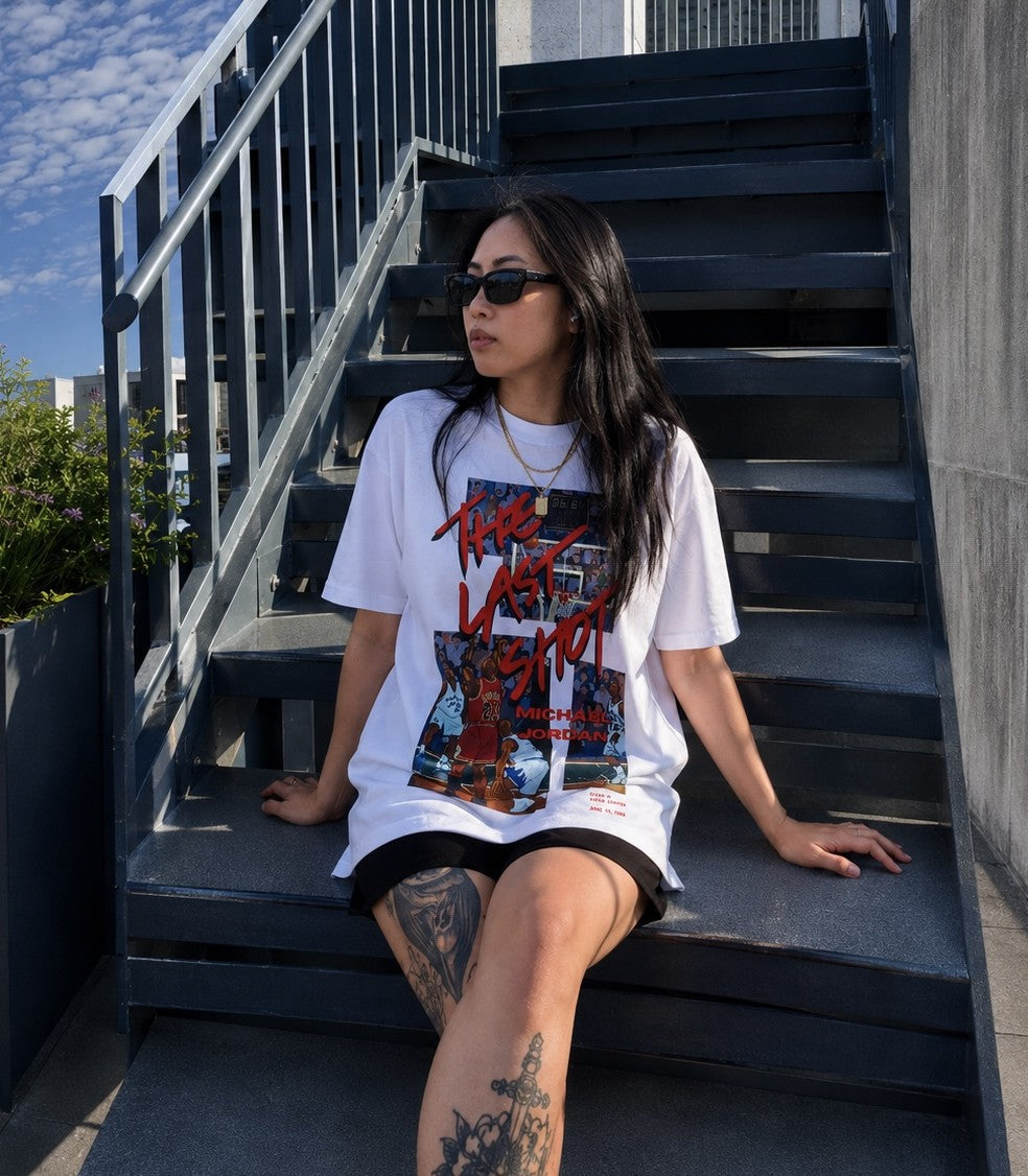 person sitting outdoors wearing The Last Shot Tee by Hai Tide, featuring original basketball-inspired artwork printed on a white heavyweight T-shirt.